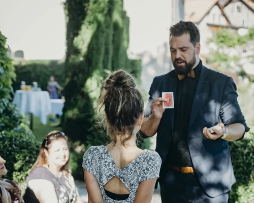 Harry Covert prÃ©sente un tour de cartes Ã  des invitÃ©es pendant une rÃ©ception en extÃ©rieur